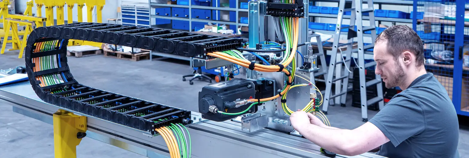 An employee is installing an automation system. Energy chains and cables are being installed with precision.