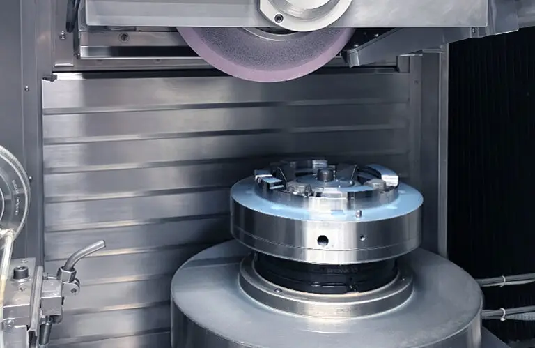 Work area of an Elb Schliff Micro Cut grinding machine with a clamped workpiece during Hirth-tooth grinding.